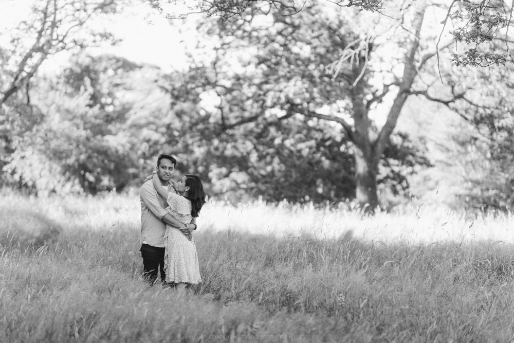 Black and white portrait of two people embracing in a dreamy field setting.
