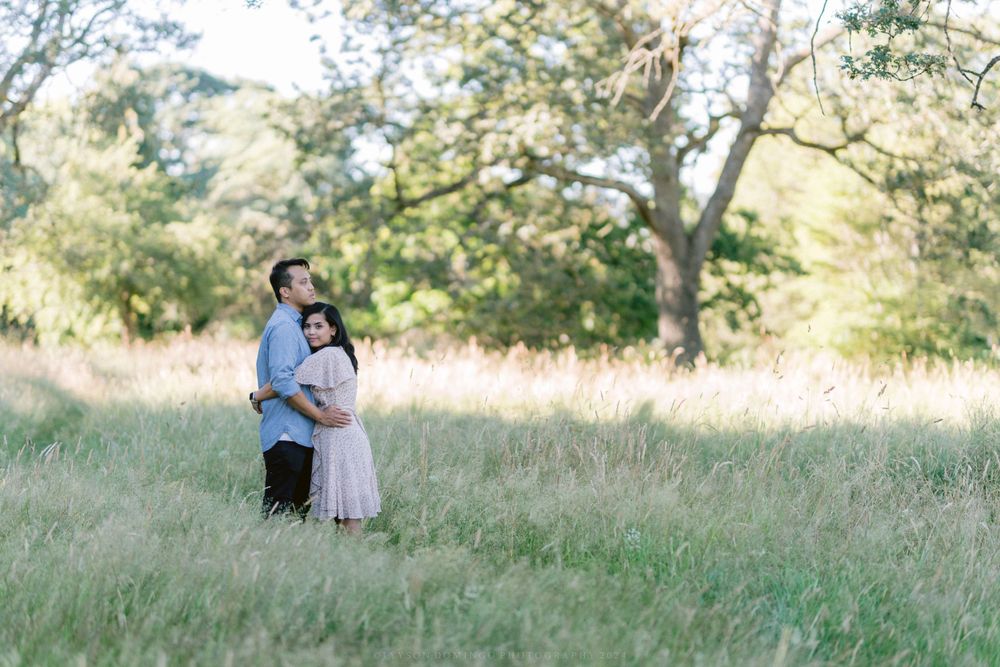 Loving couple standing together in tall grass with oak trees in the background.
