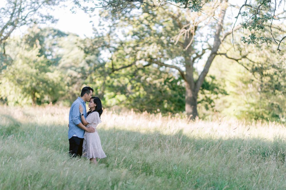 Couple sharing an intimate moment in a sun-filled meadow with oak trees.