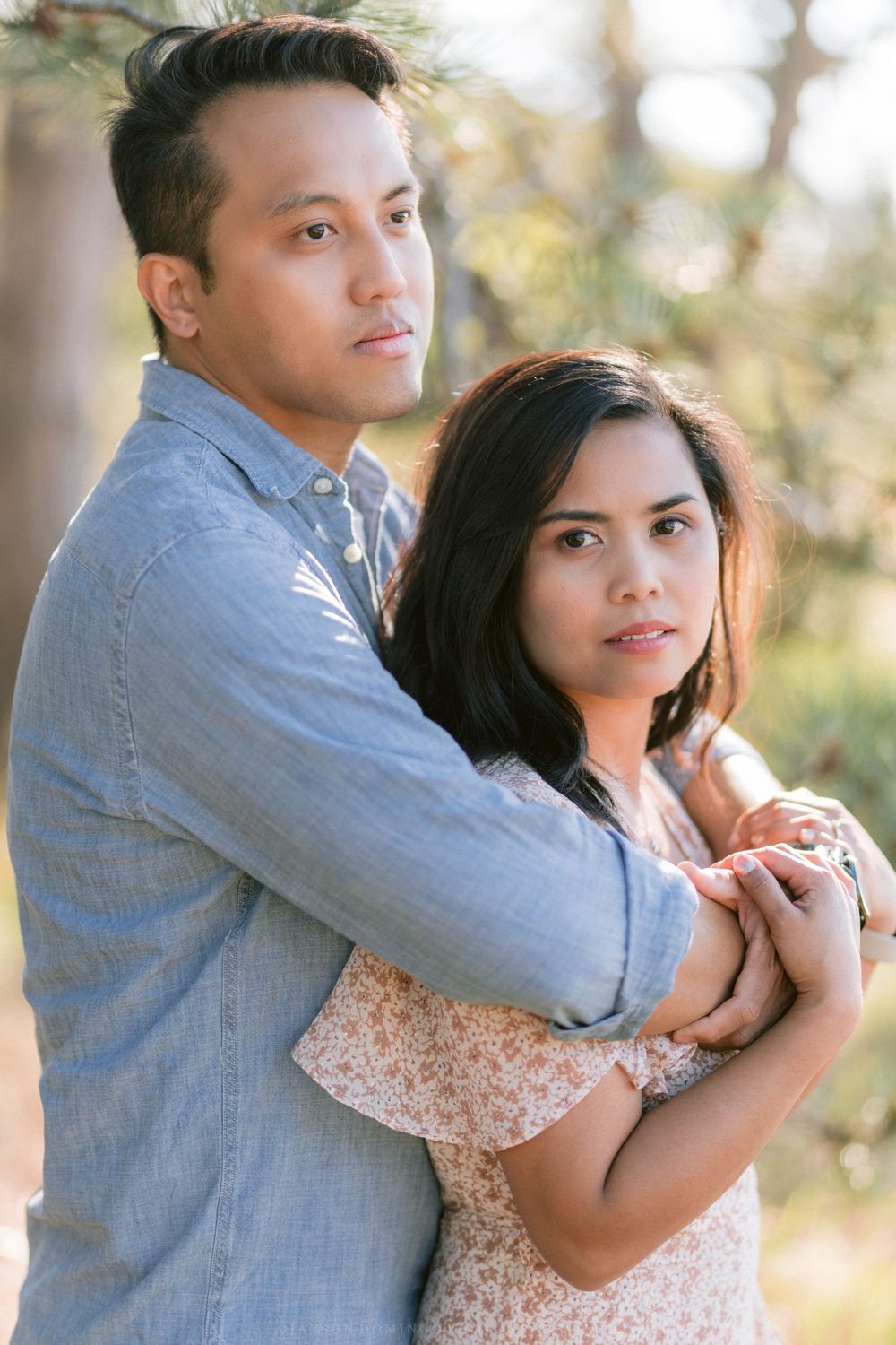 A couple shares an intimate moment while posing for engagement photos in a park.