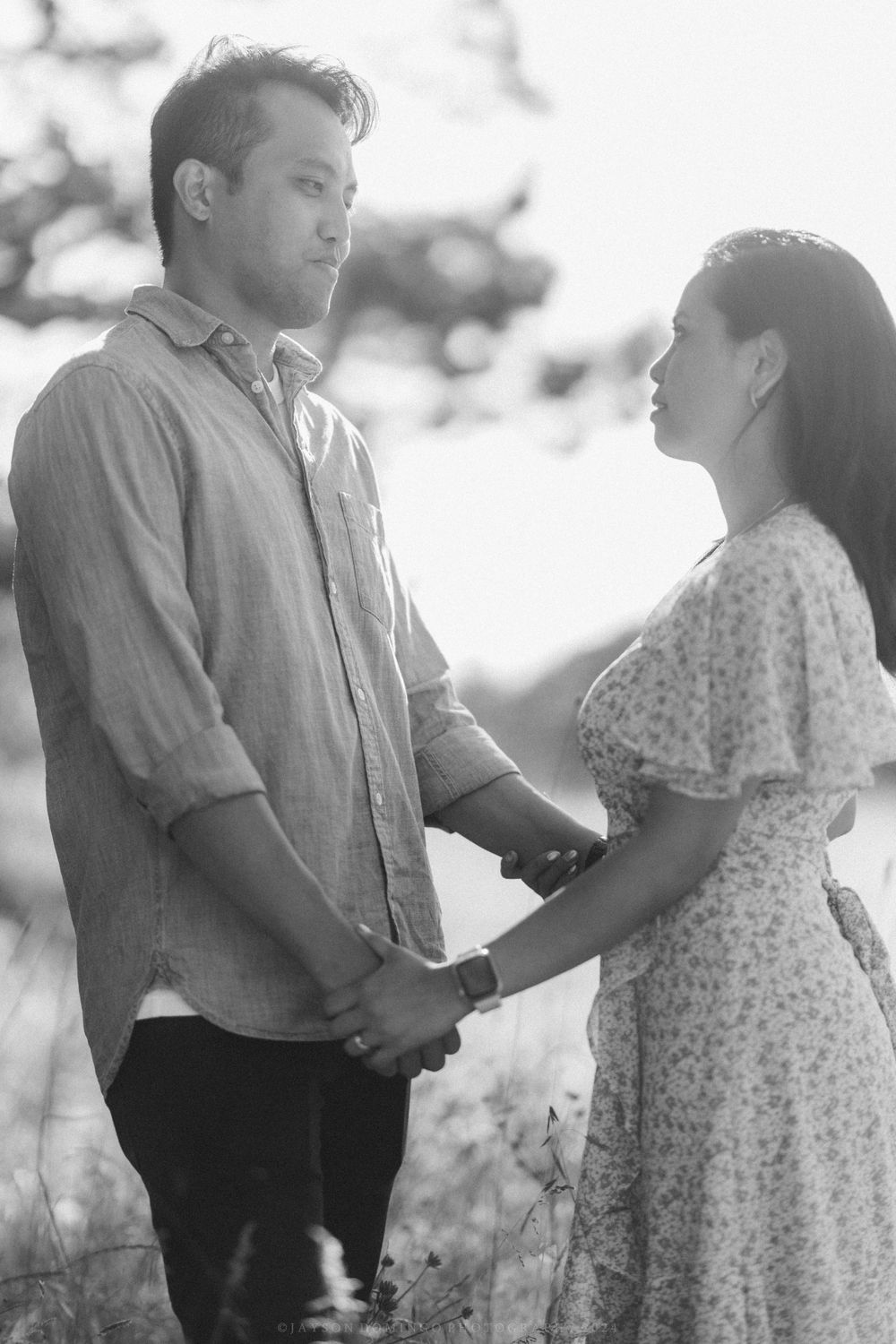 Black and white portrait of a couple holding hands and gazing at each other outdoors.