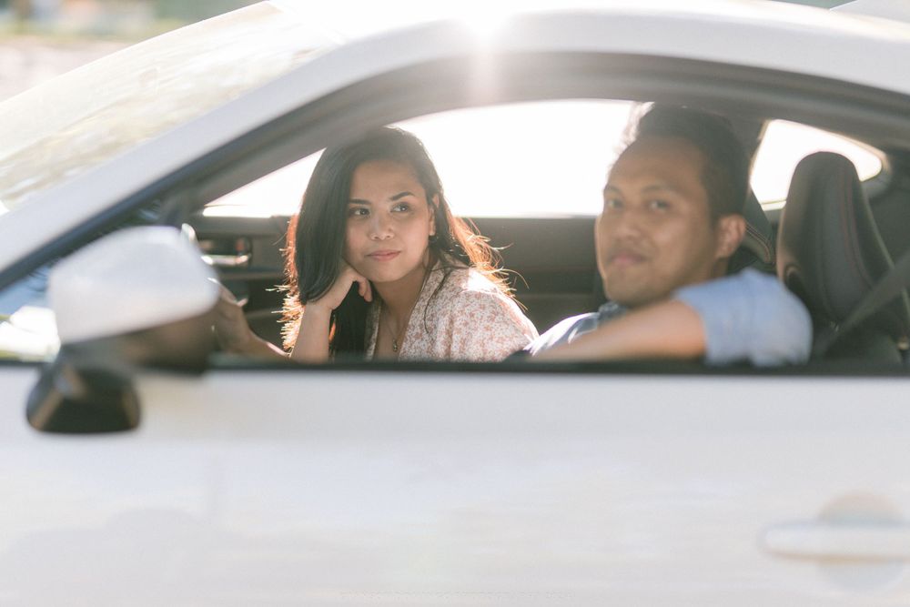 A couple sits inside a white sports car, captured through the driver's side window.