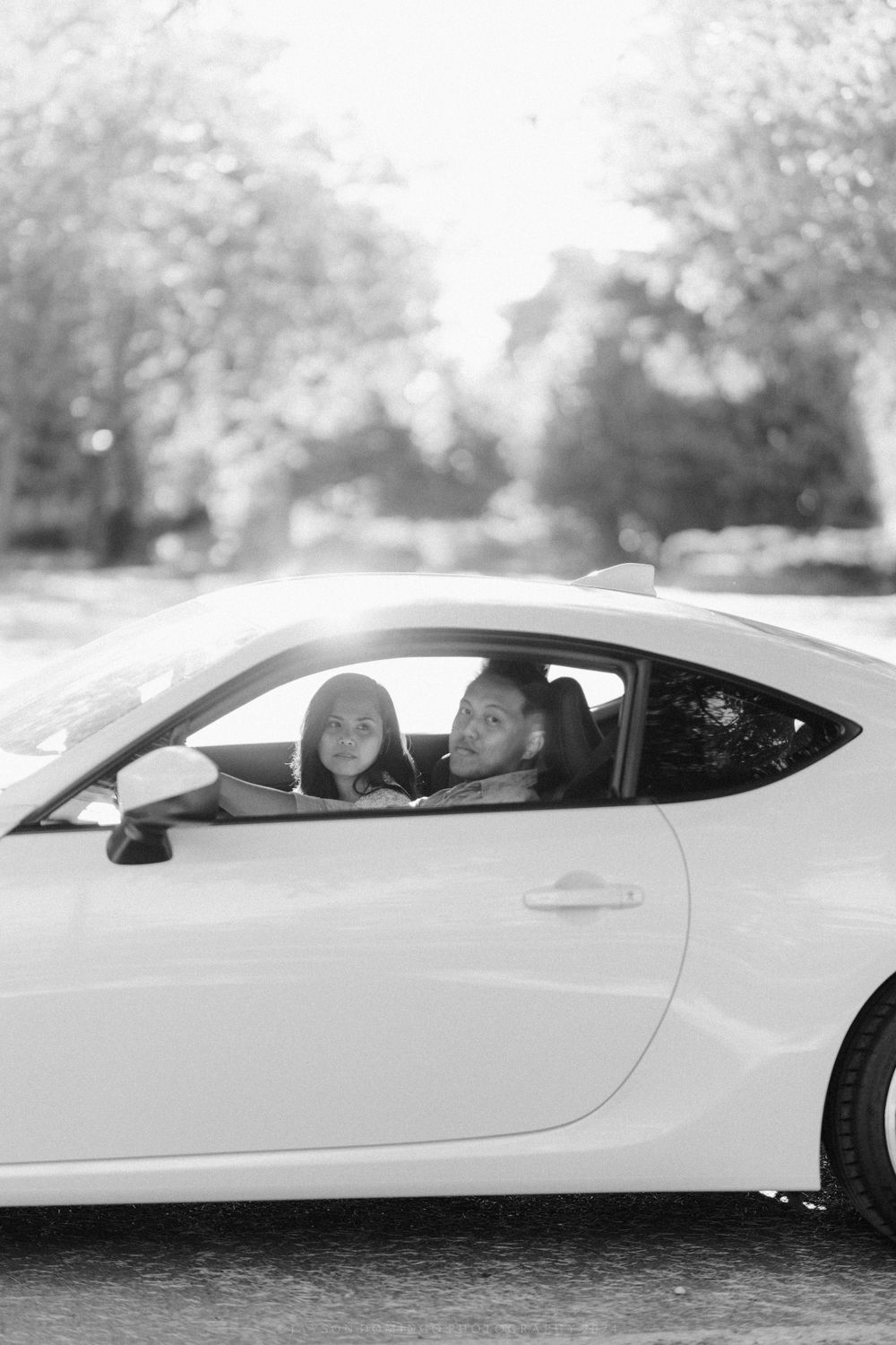 A white sports car with passengers photographed in black and white against a blurred natural background.