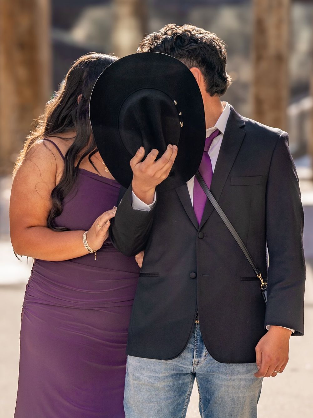 Couple poses together with black hat covering their faces in romantic portrait.