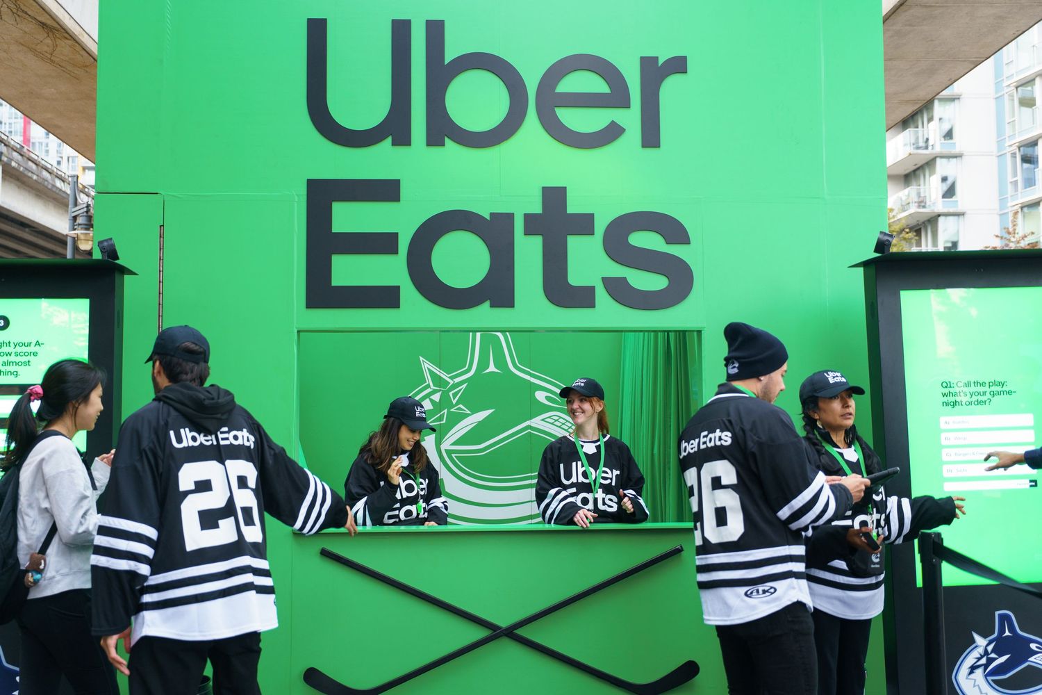 A series of Uber Eats delivery drivers waiting in line against a bright green wall with the Uber Eats logo.