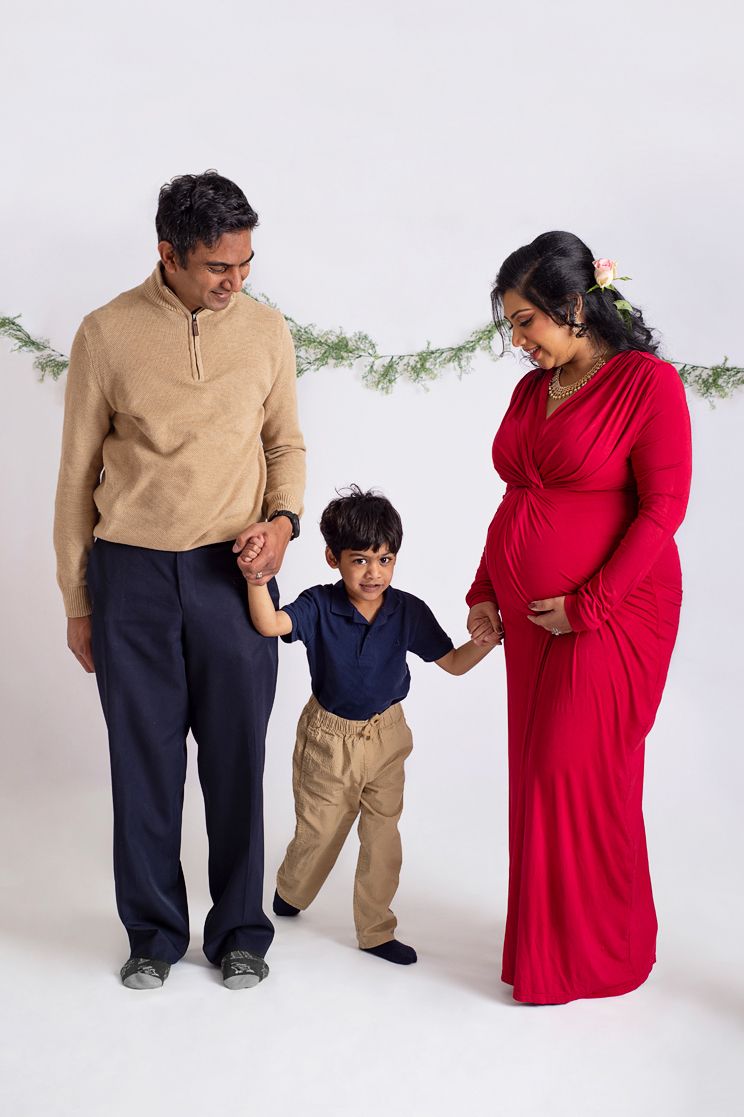 Happy family Full body portrait of pregnant mother in red dress holds hands with husband and son smiling at each other
