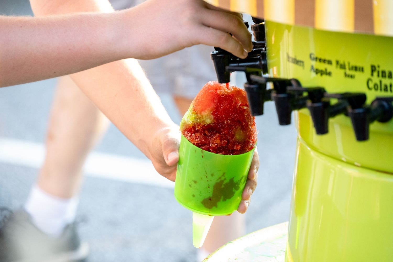 Hand pouring a bright red slushie drink into lime green cup from dispenser.