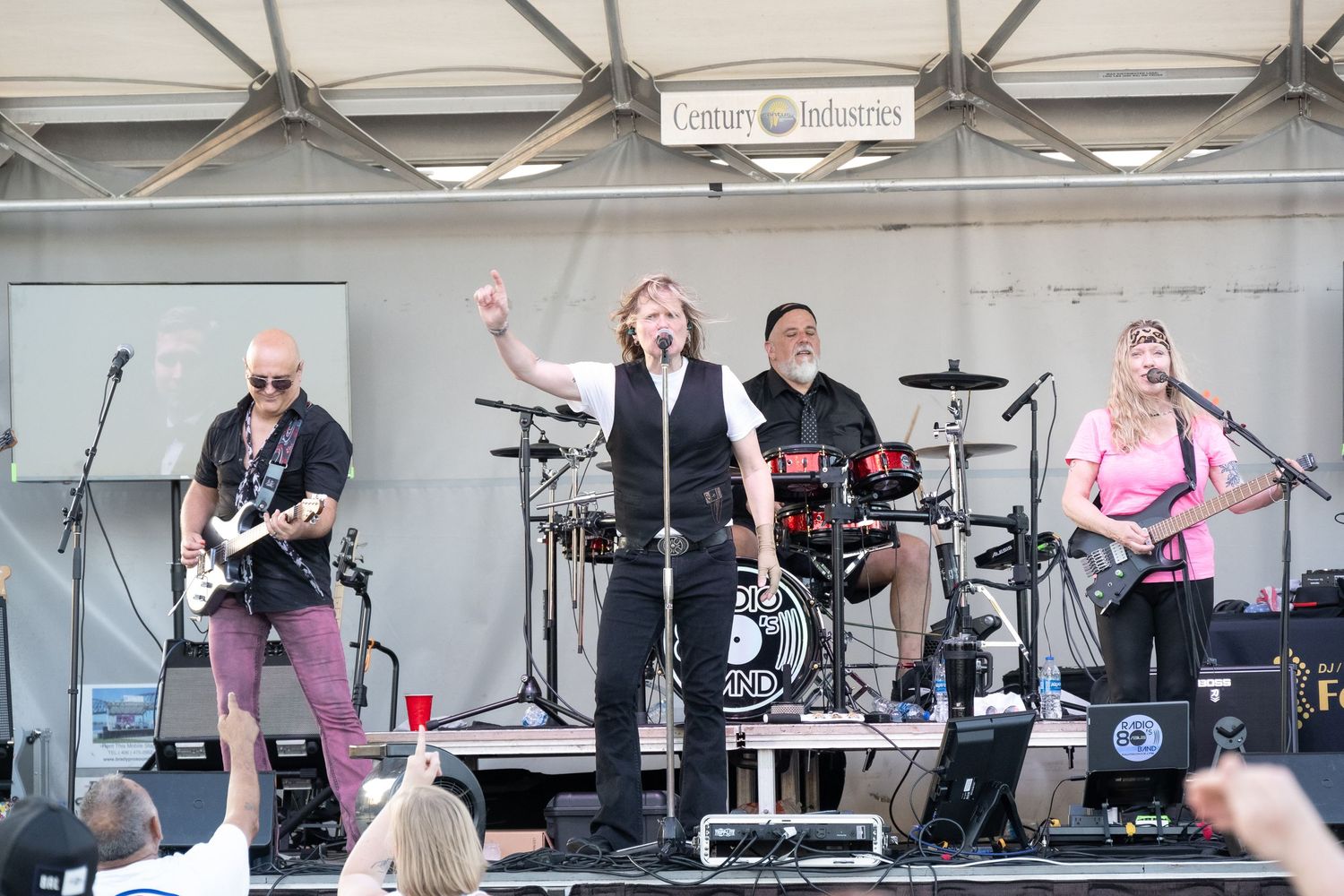 Rock band performs energetically on outdoor stage at Century Industries event.