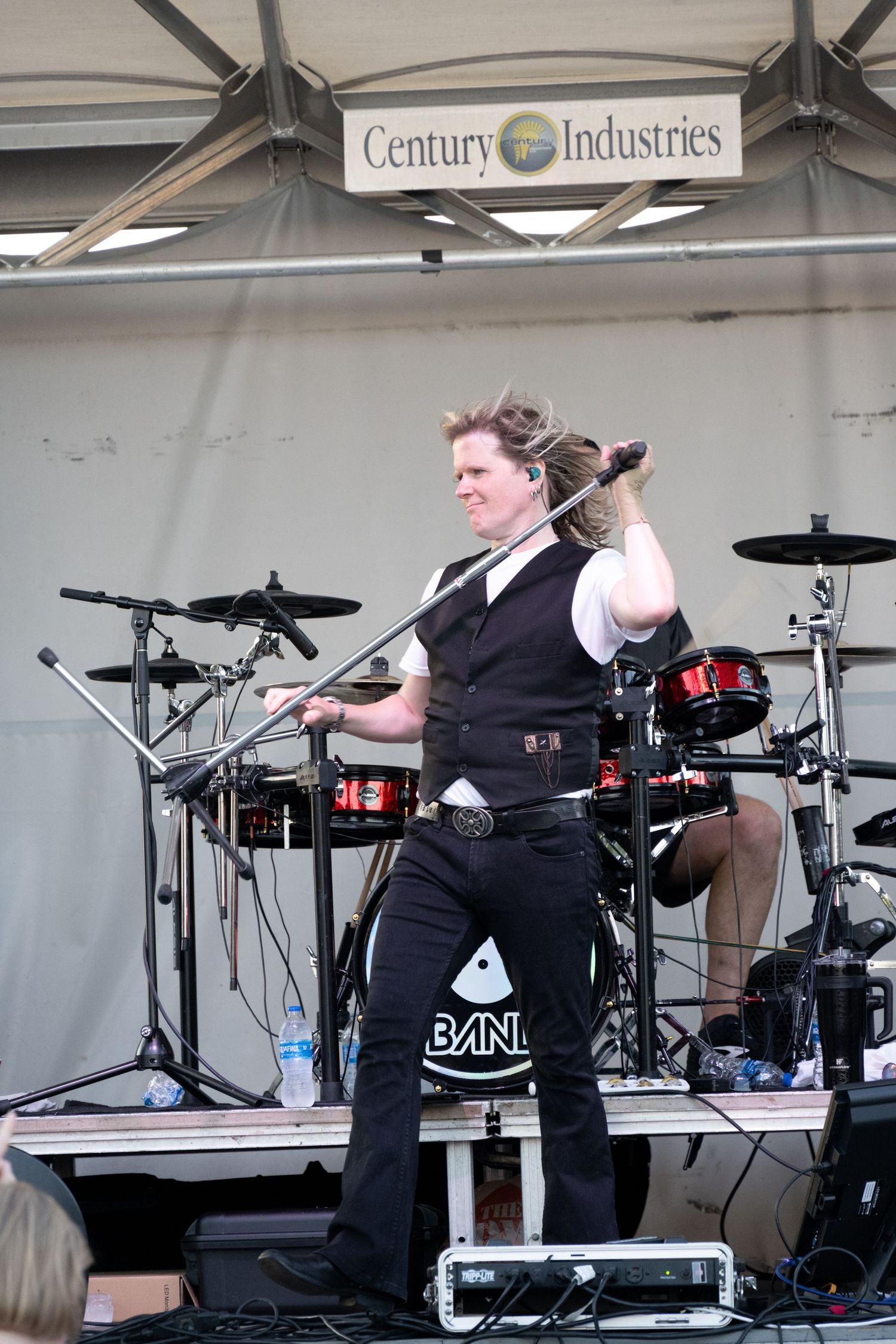 Performer in black vest on stage with drum kit and microphone.