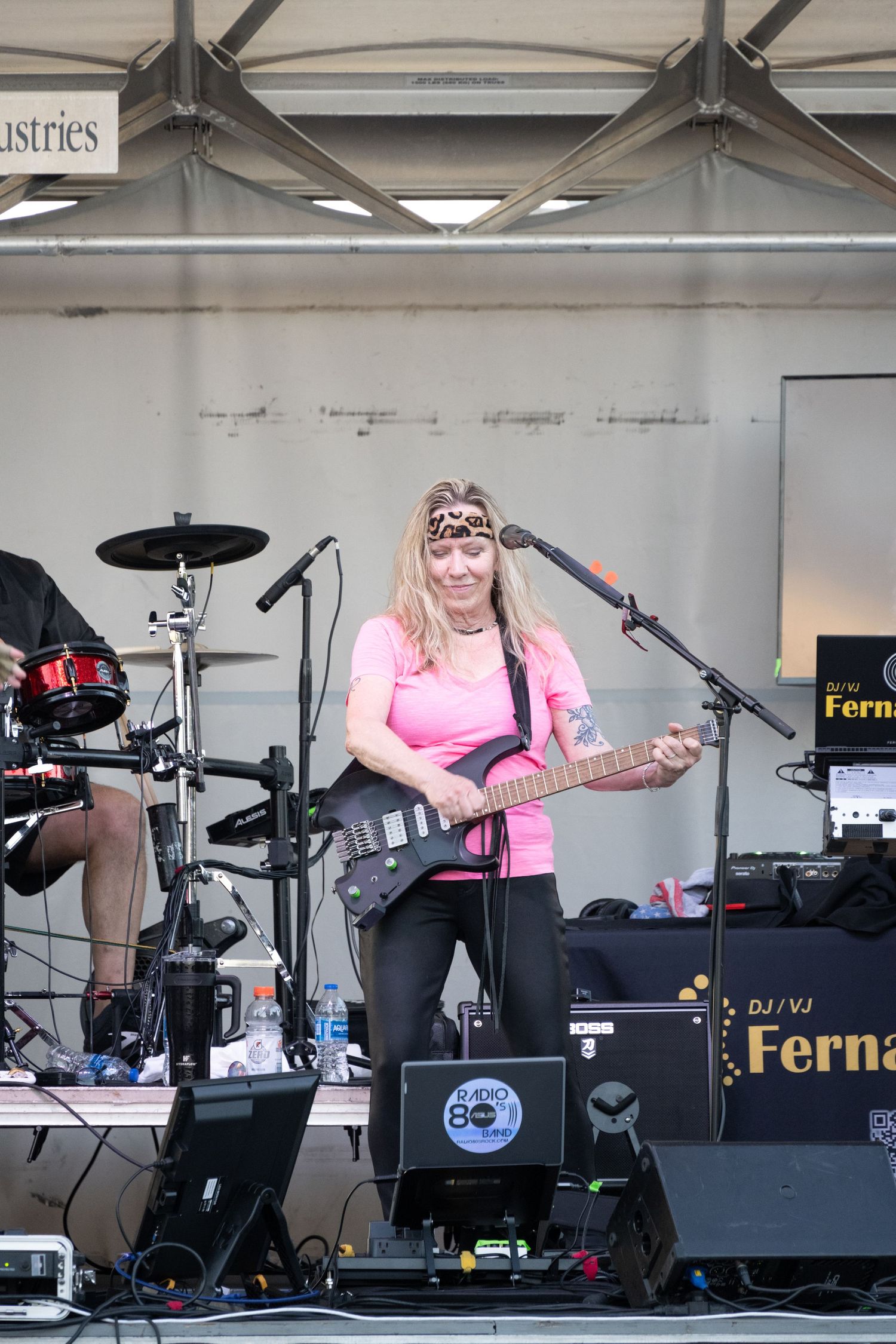 Bass guitarist in bright pink shirt performs on festival stage with equipment.