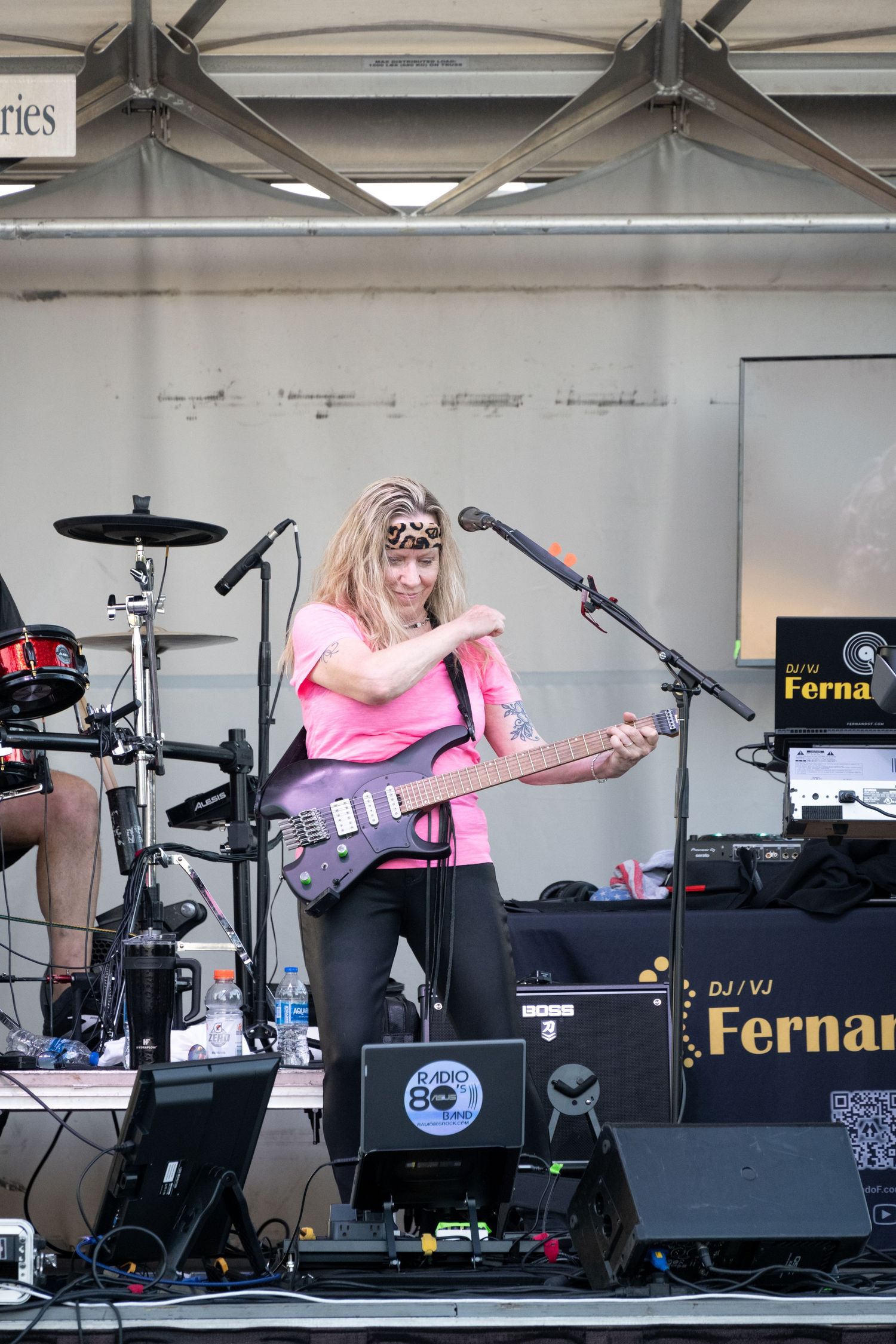 Musician in pink shirt playing bass guitar on outdoor festival stage.
