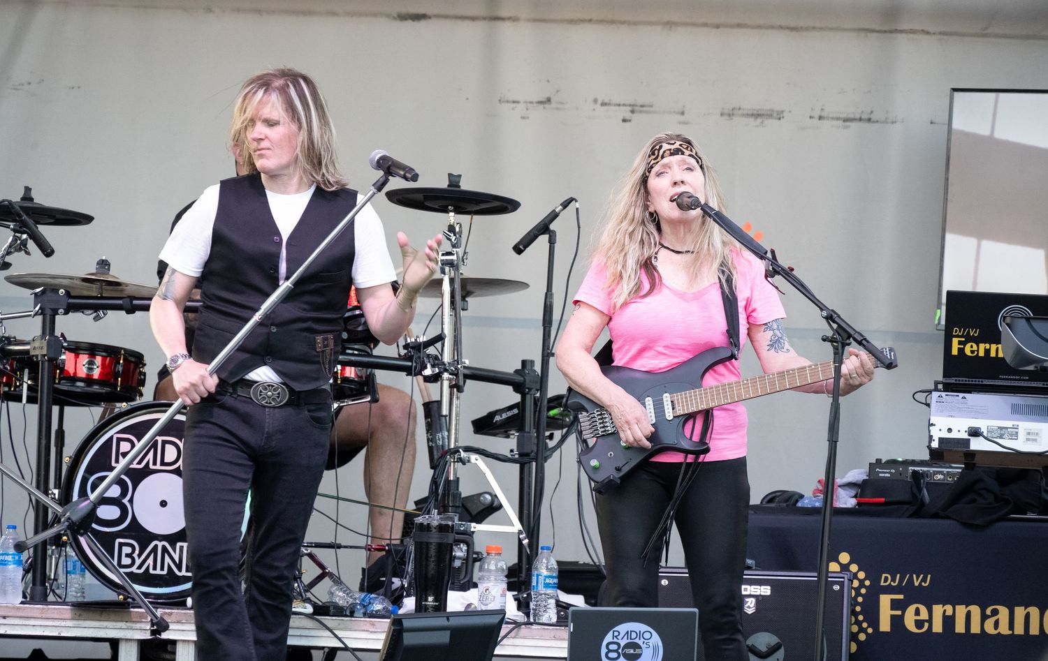 Band members performing with guitars and drums on outdoor festival stage setup.