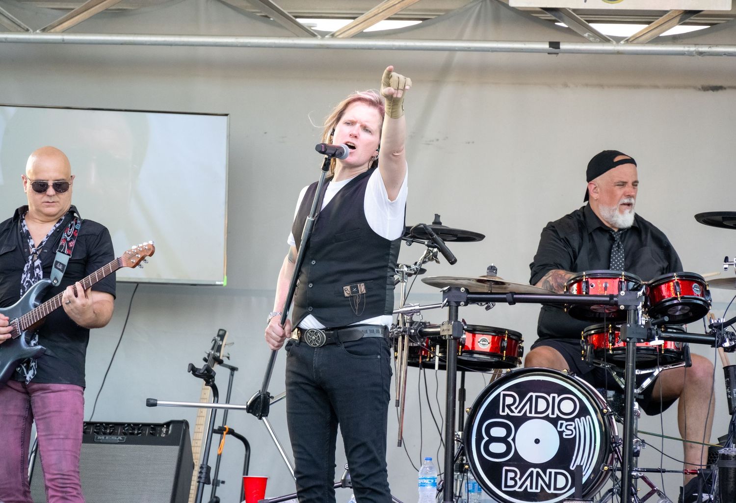 Live band performs with guitar and drums featuring Radio 80s Band logo on stage.