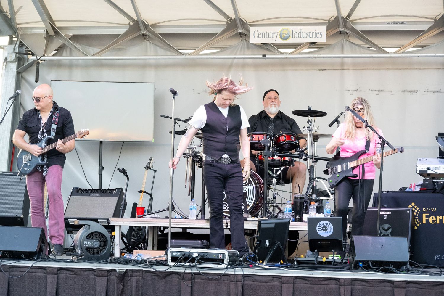 Full band setup on an outdoor stage with various instruments and equipment under a white canopy.