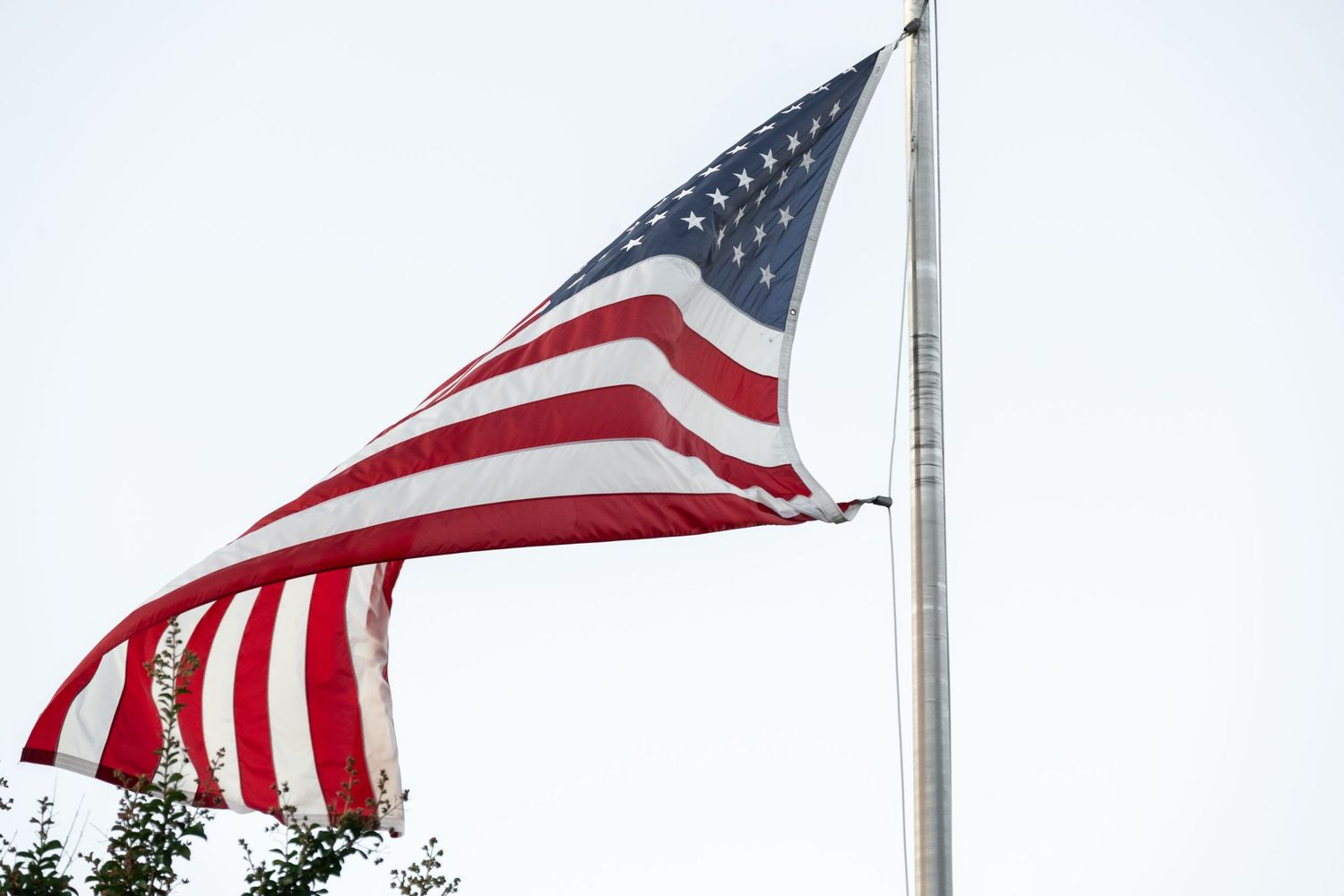 Large American flag flying on tall pole against white cloudy sky.
