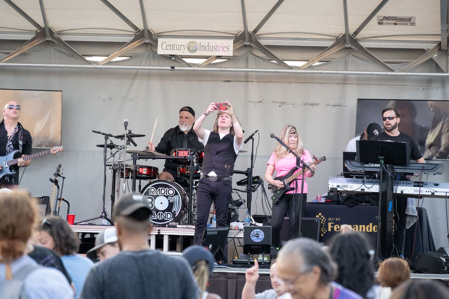 Band performing on outdoor stage with crowd visible below during daytime event.