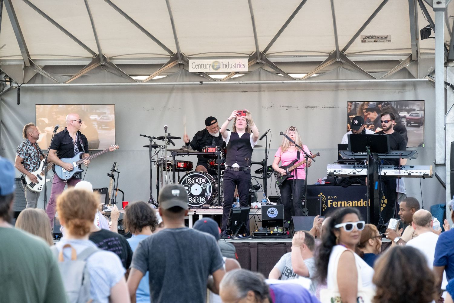 Wide shot of band performing on elevated stage with audience members watching below.