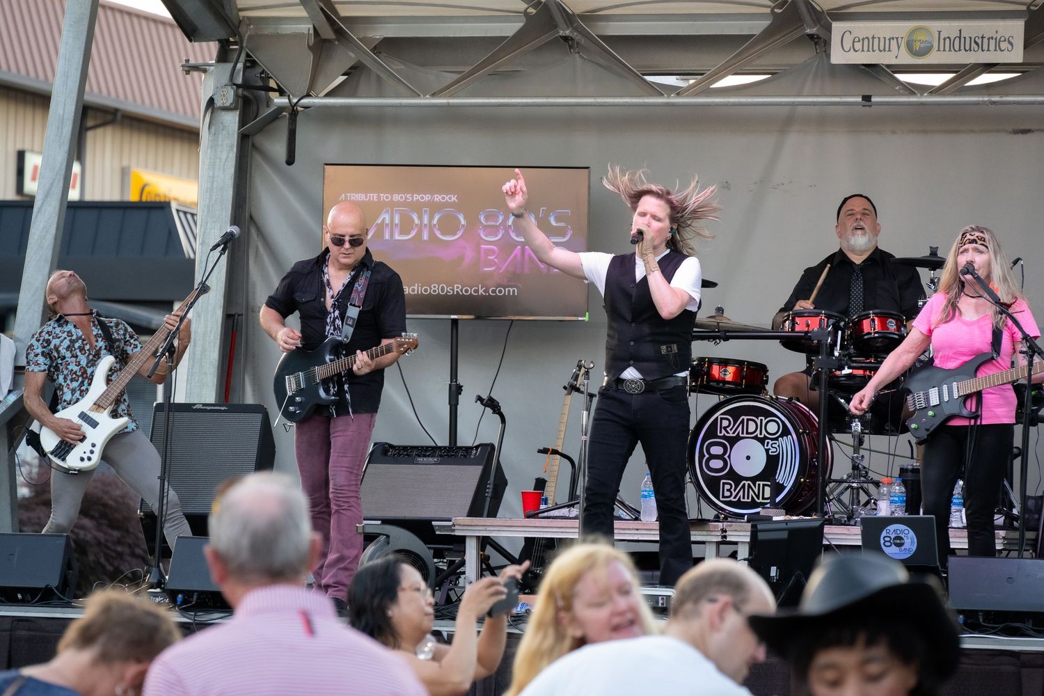 Rock band performing on stage at an outdoor music festival with audience visible in foreground.