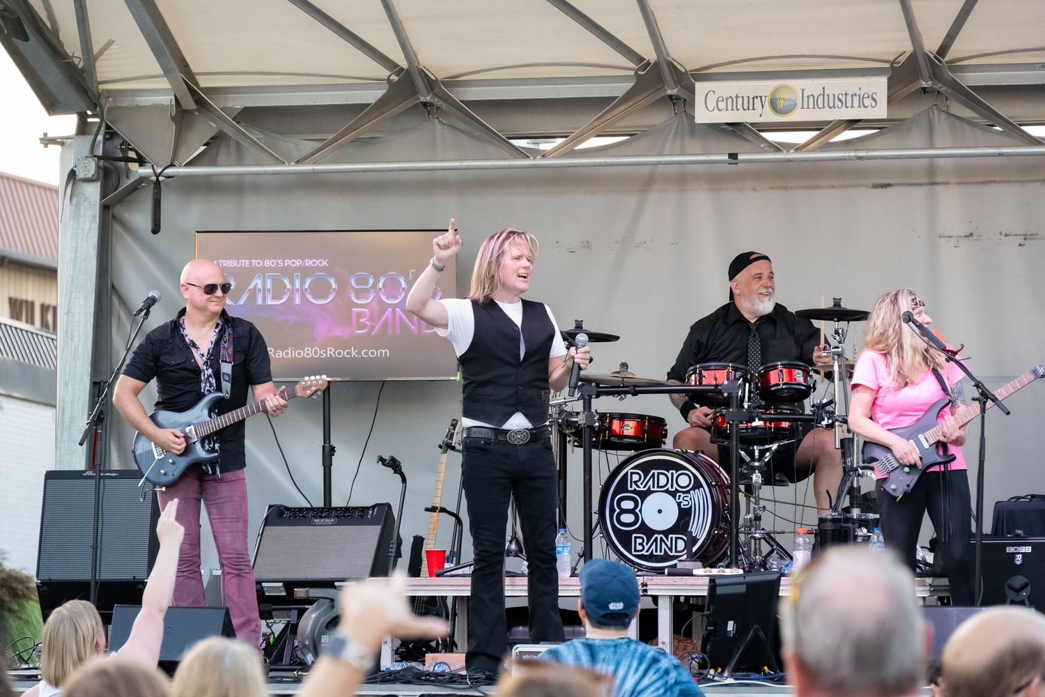 Musical group performing under a covered stage with audio equipment and lighting setup.