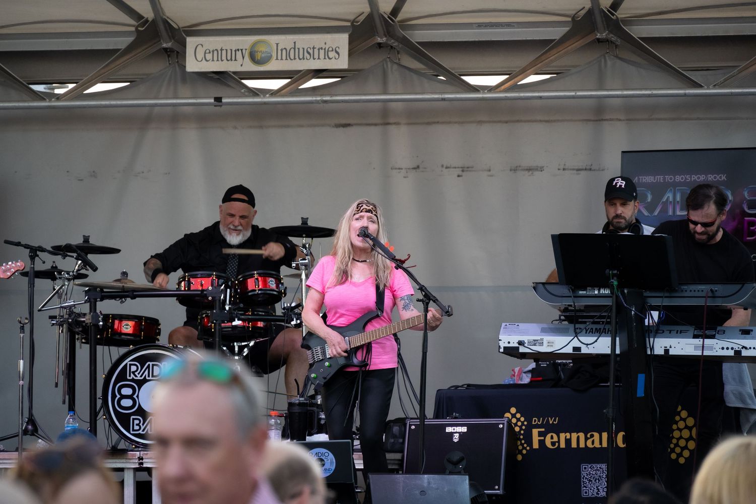 Live music performance featuring drums, guitar and vocals on an outdoor festival stage.
