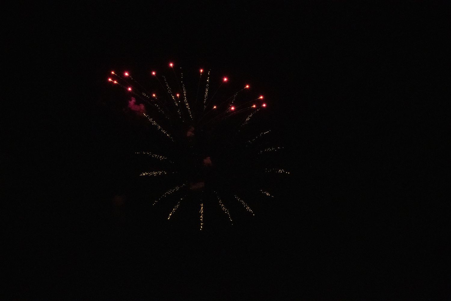 Red and gold firework explosion creating circular pattern in dark sky.