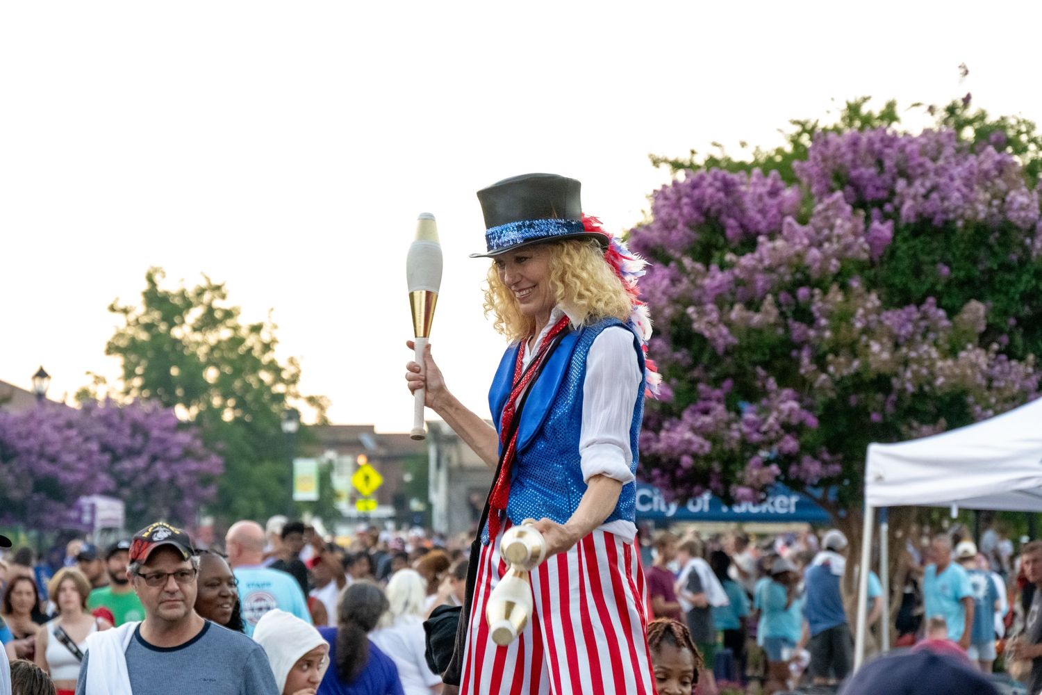 A performer in patriotic attire juggles while entertaining crowds at an outdoor festival.
