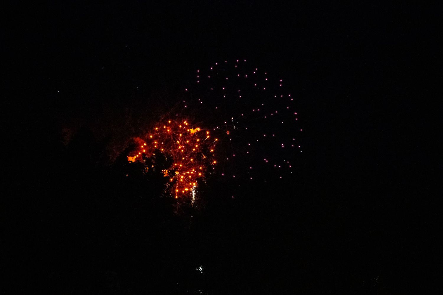 Multiple red fireworks bursts light up the night sky simultaneously.