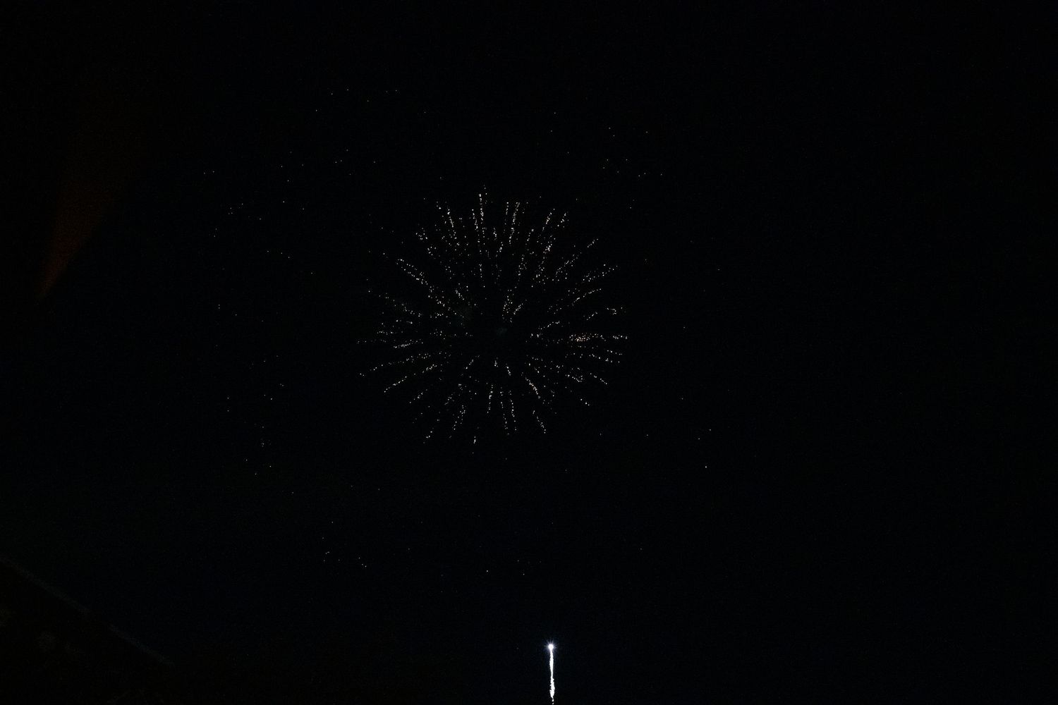 A faint white firework burst illuminates the night sky with delicate trails.