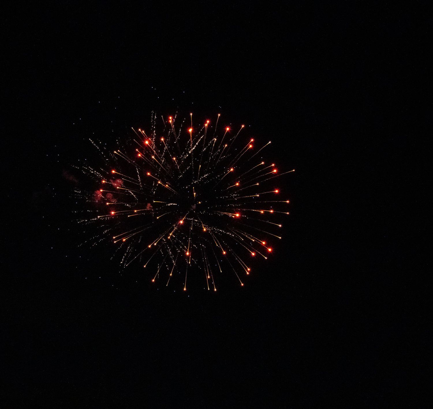 Red firework bursts into a perfect sphere of glowing points against dark background.