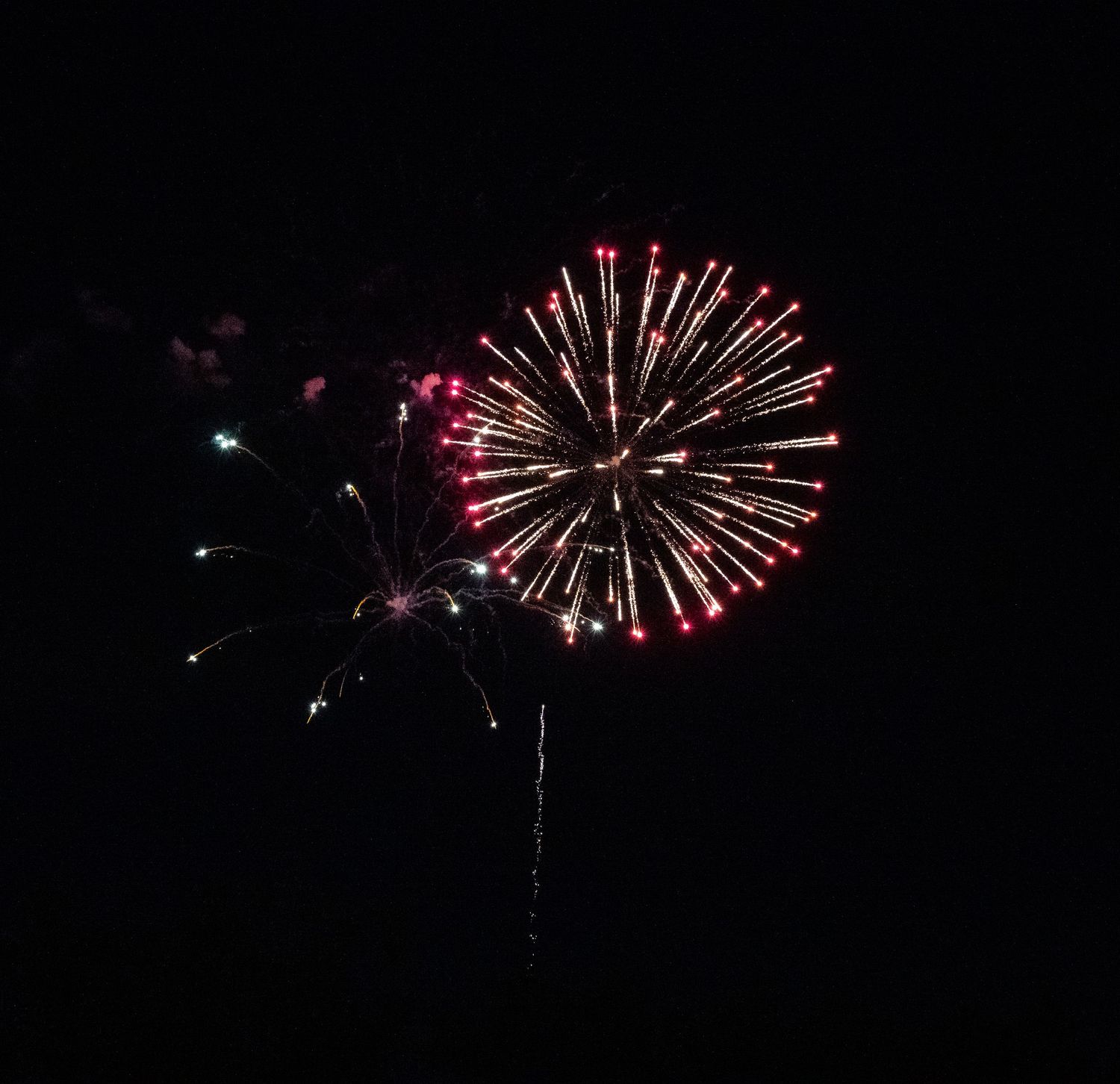 Vibrant red and white firework burst creates a dramatic spherical pattern against the night sky.