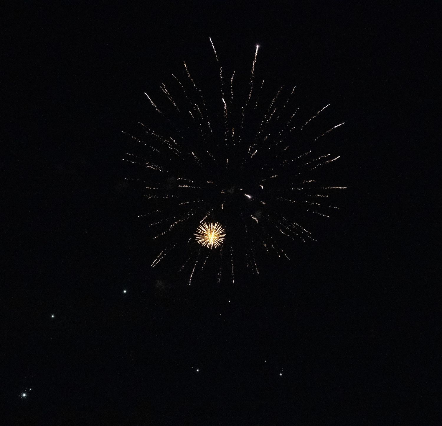Double firework display with large white starburst above smaller golden burst against black sky.