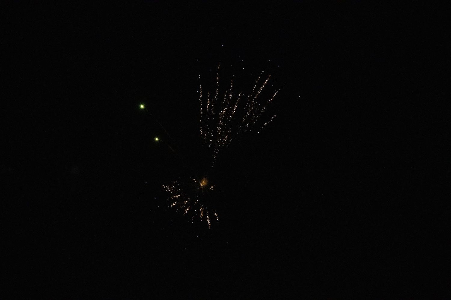 Small golden firework burst against dark night sky with green sparkles.
