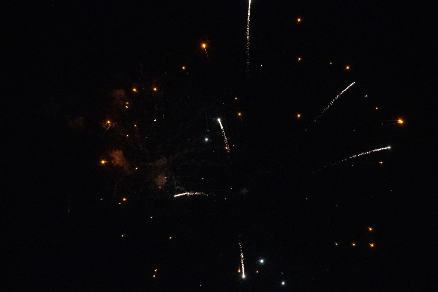 Orange and white fireworks creating streaking patterns across the night sky.