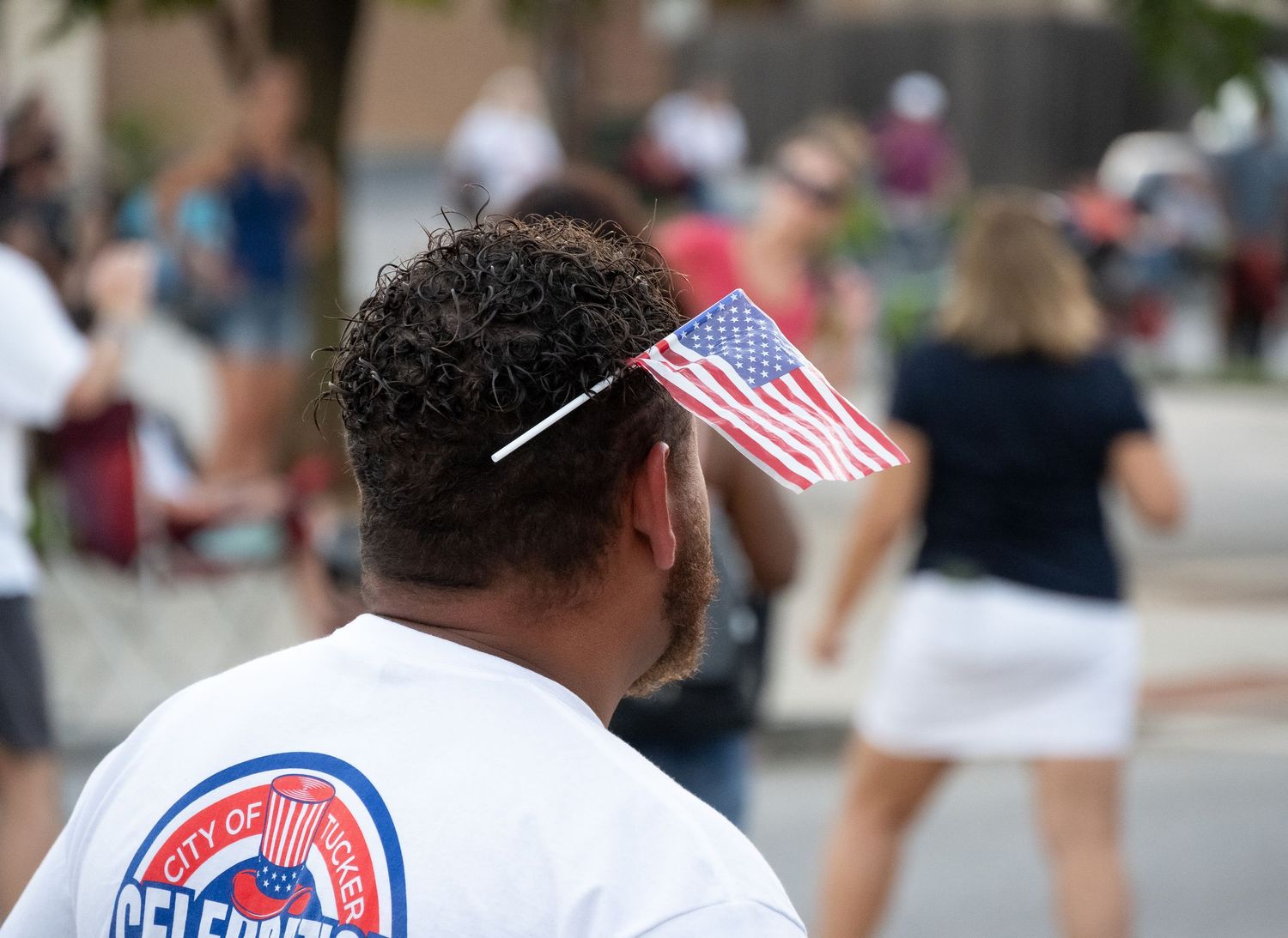 Spectator in white shirt with small American flag watching parade.