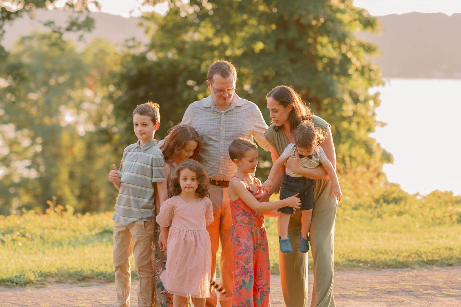 A family gathers together outdoors during golden hour with water and trees in background.