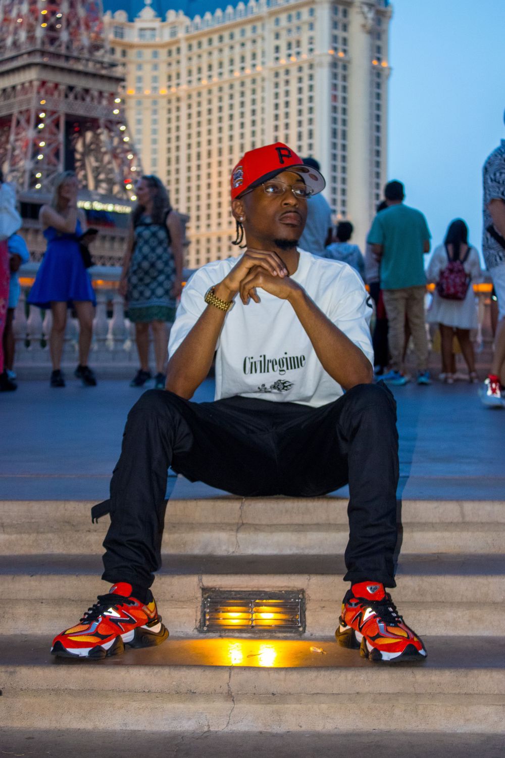Man in red cap and Civilregime tee sits on steps with Paris Las Vegas in background.