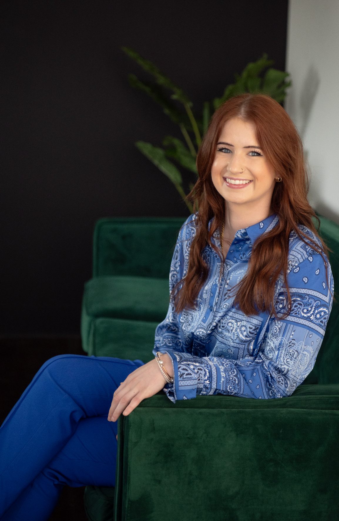 Portrait of woman in blue patterned shirt sitting on emerald green velvet chair.