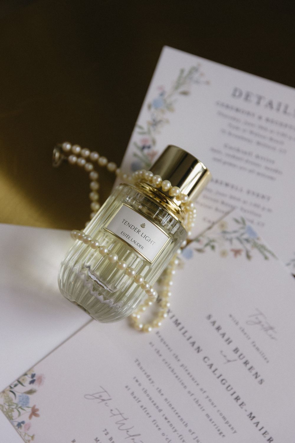 Wedding invitation details with a perfume bottle and pearl accessories on white paper.
