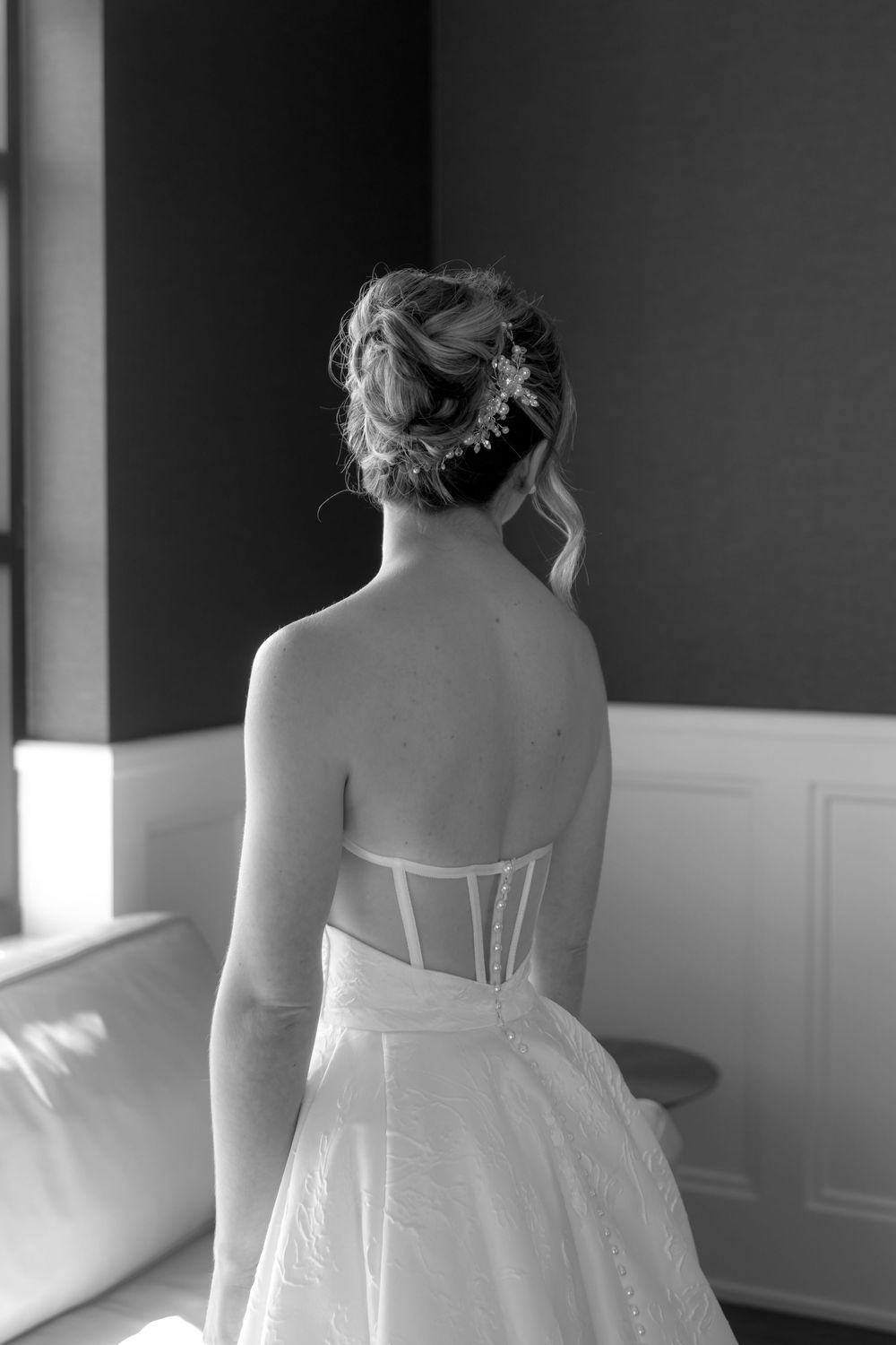 Back view of an elegant white wedding dress with corset details in a sunlit room.