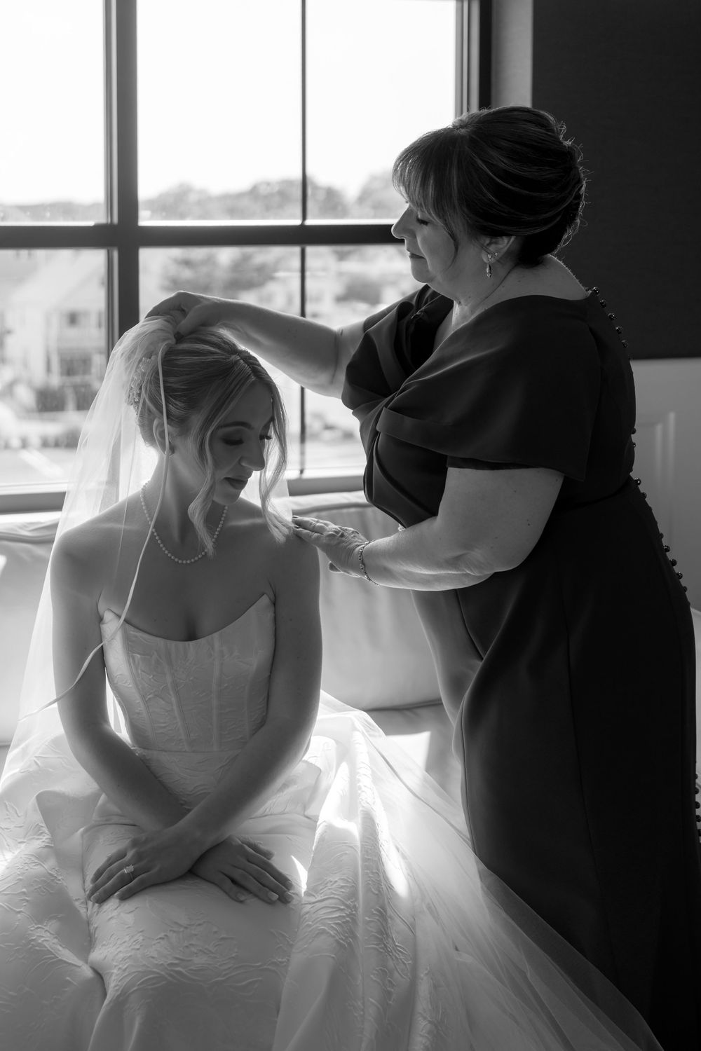 Black and white photo of wedding dress preparations in a sunlit room.