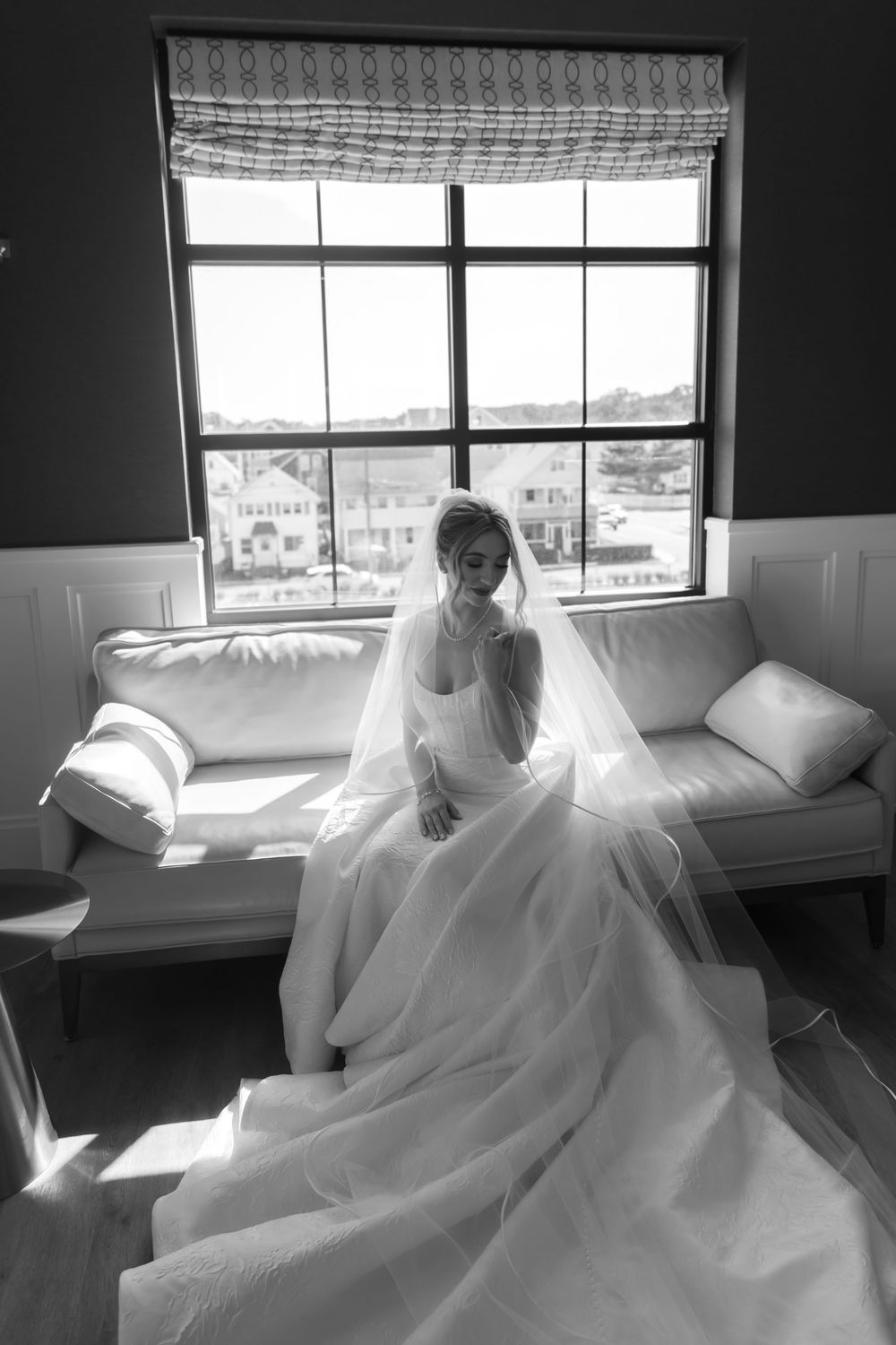 Artistic black and white photo of a bride sitting by windows with natural light streaming in.