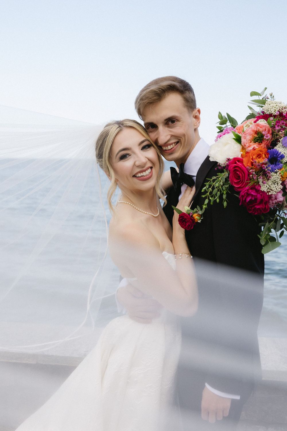 Seaside wedding portrait with colorful bouquet against ocean backdrop.