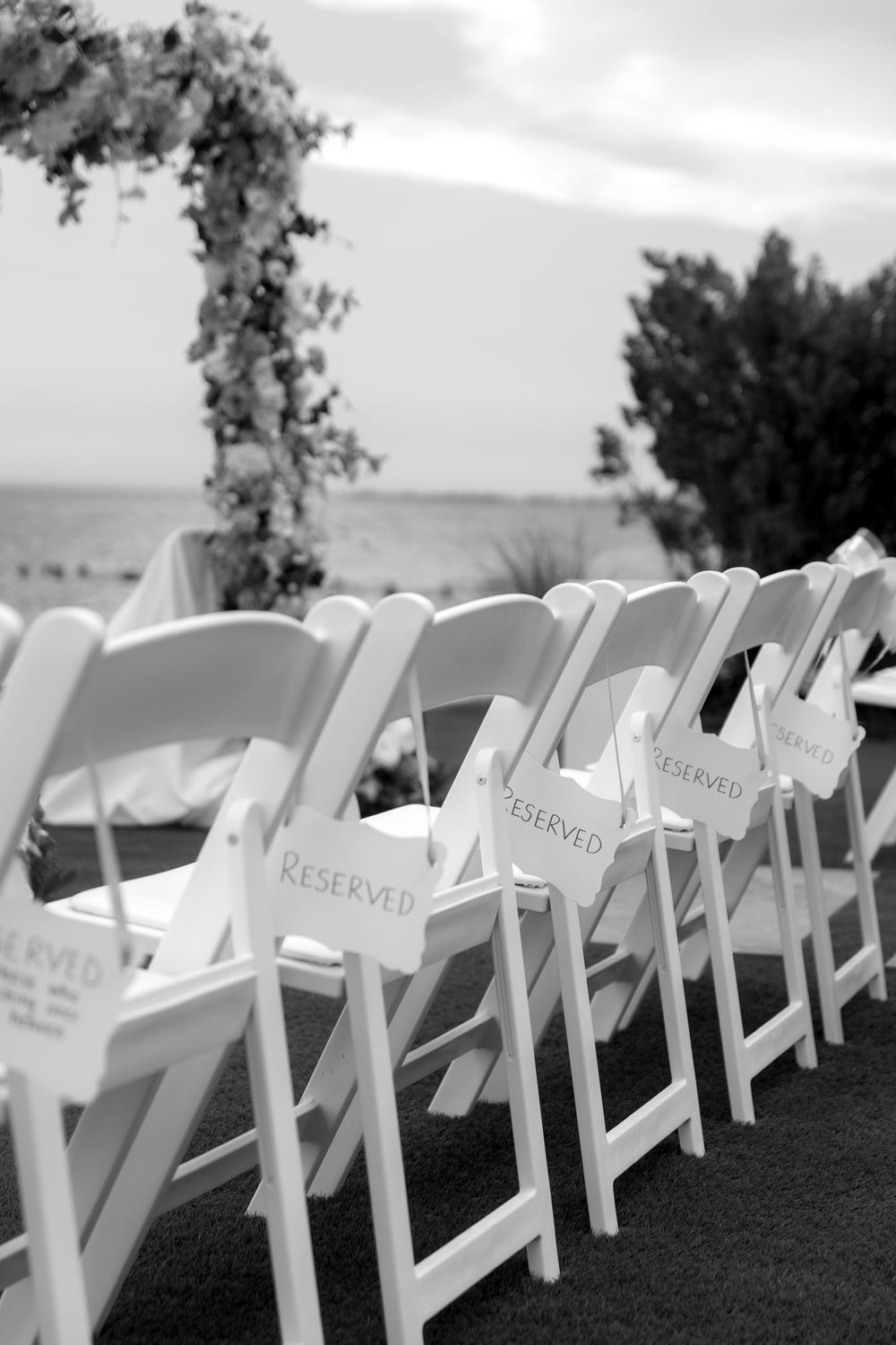 Row of white folding chairs with reserved signs set up for an outdoor wedding ceremony.