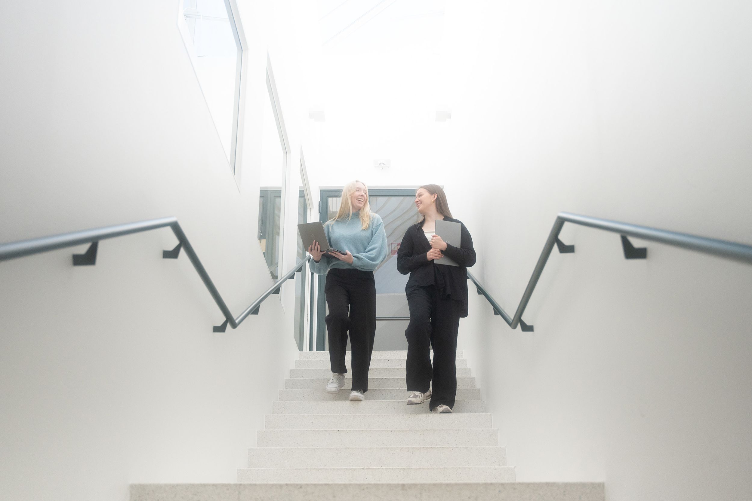 Two people walking up white stairs with metal handrails in a minimalist setting.