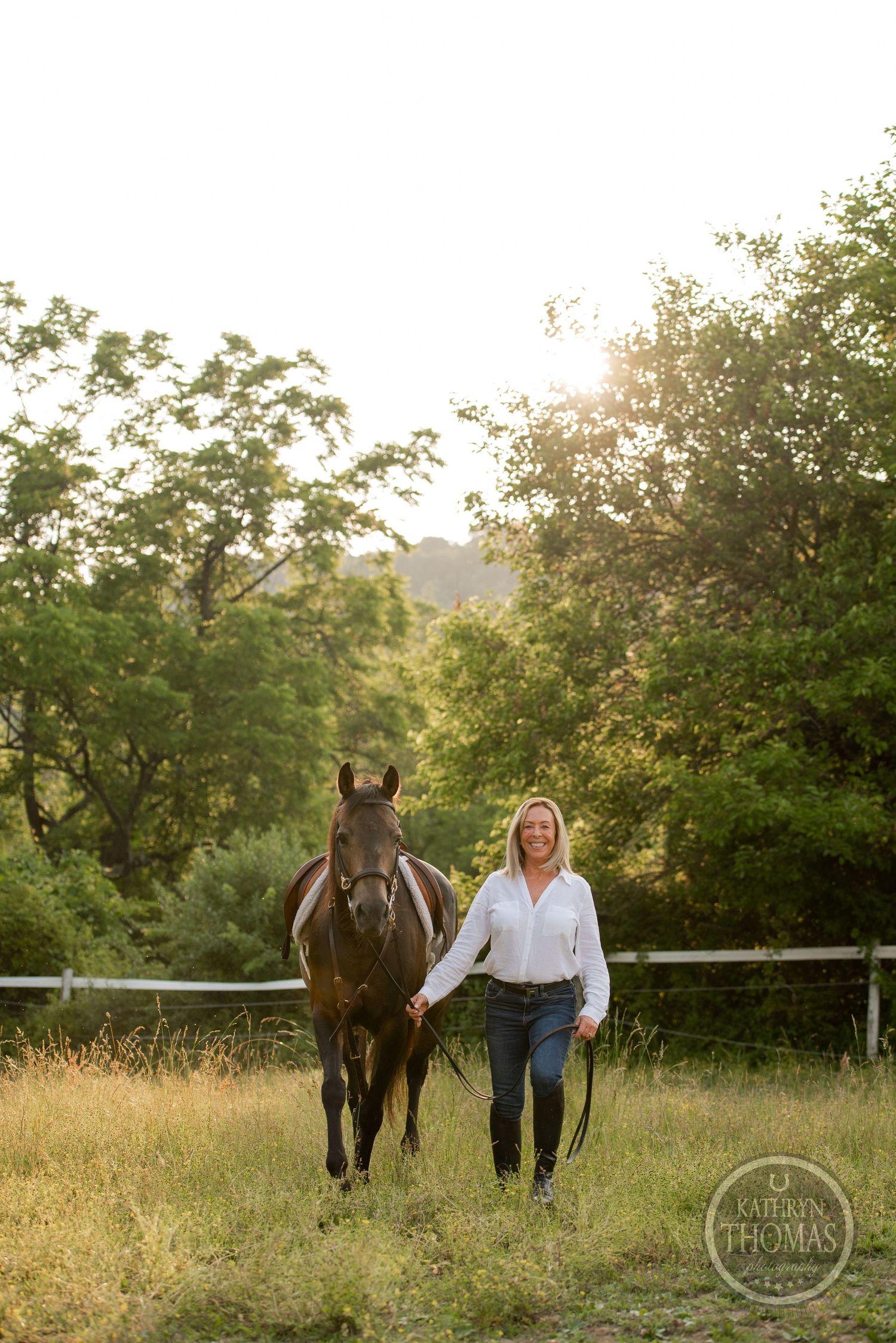 A beautiful bay horse and companion walking together through a sunlit pasture with trees.