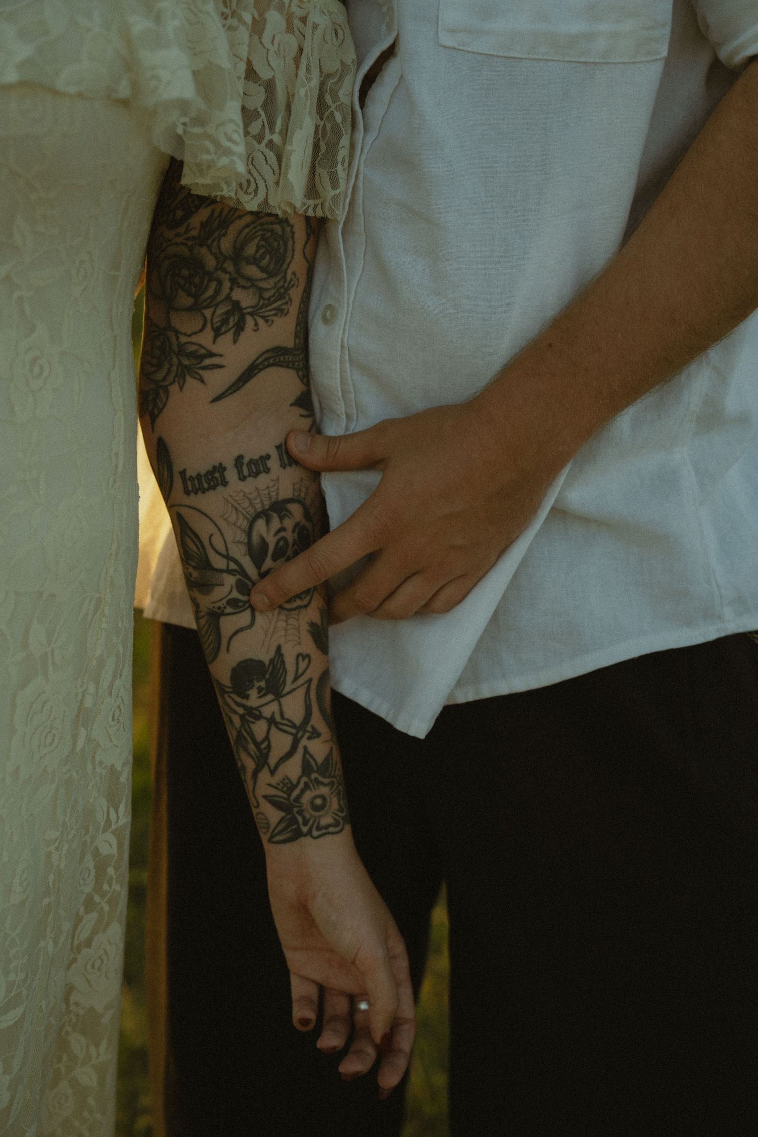 Close-up of a tattooed arm with intricate black and grey floral sleeve design against white clothing.