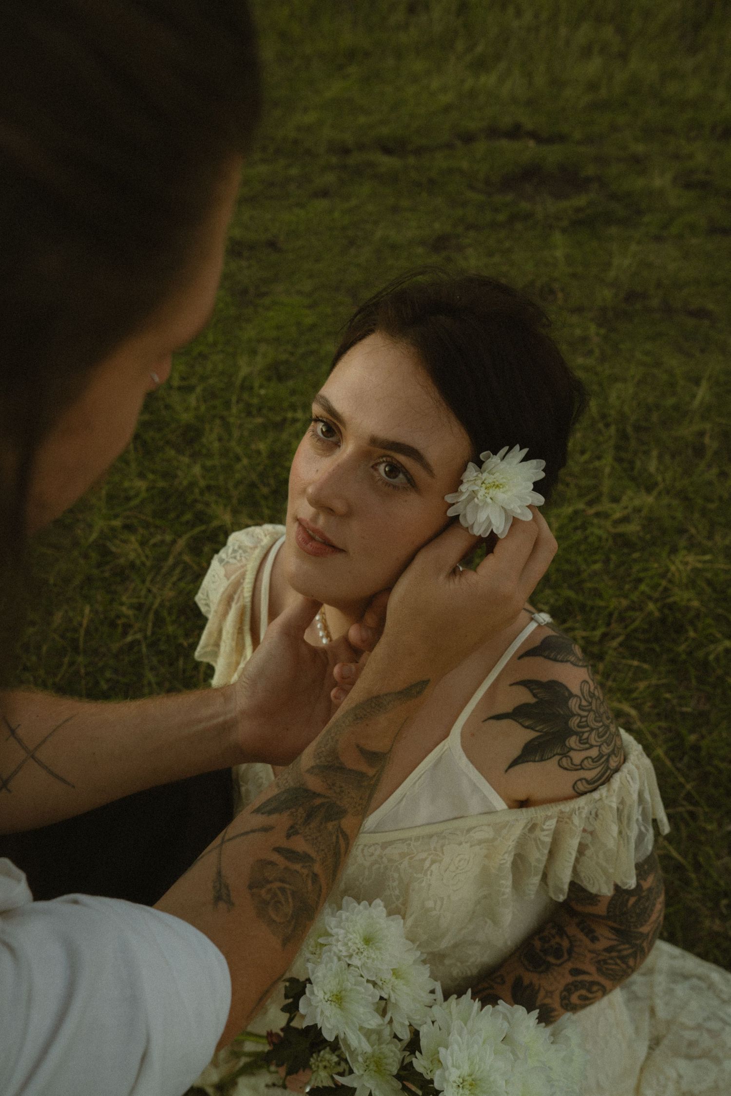 A romantic wedding photoshoot in a grassy field with white floral decorations and delicate styling.
