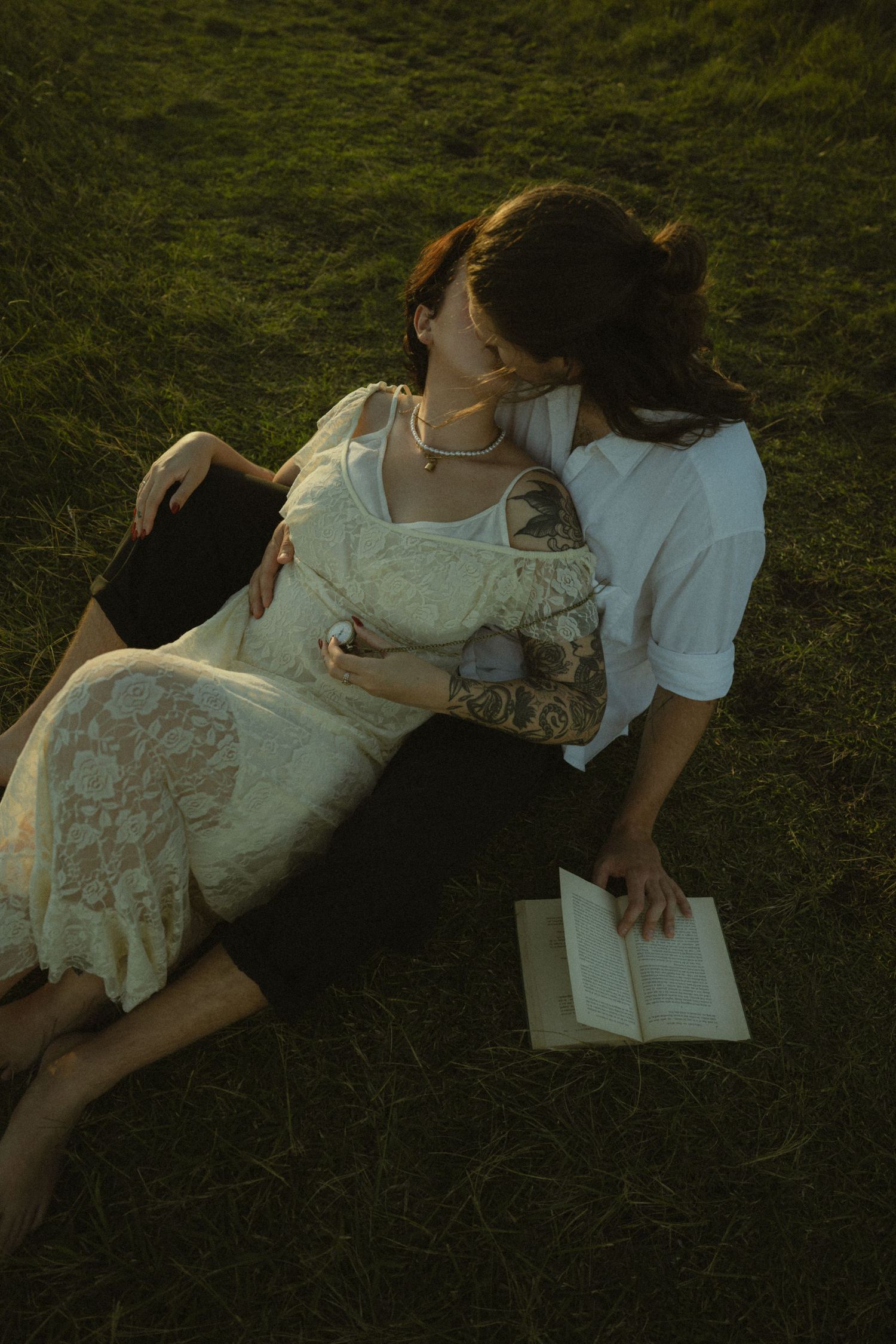 Two people lying on grass reading a map together in vintage white dresses on a summer afternoon.