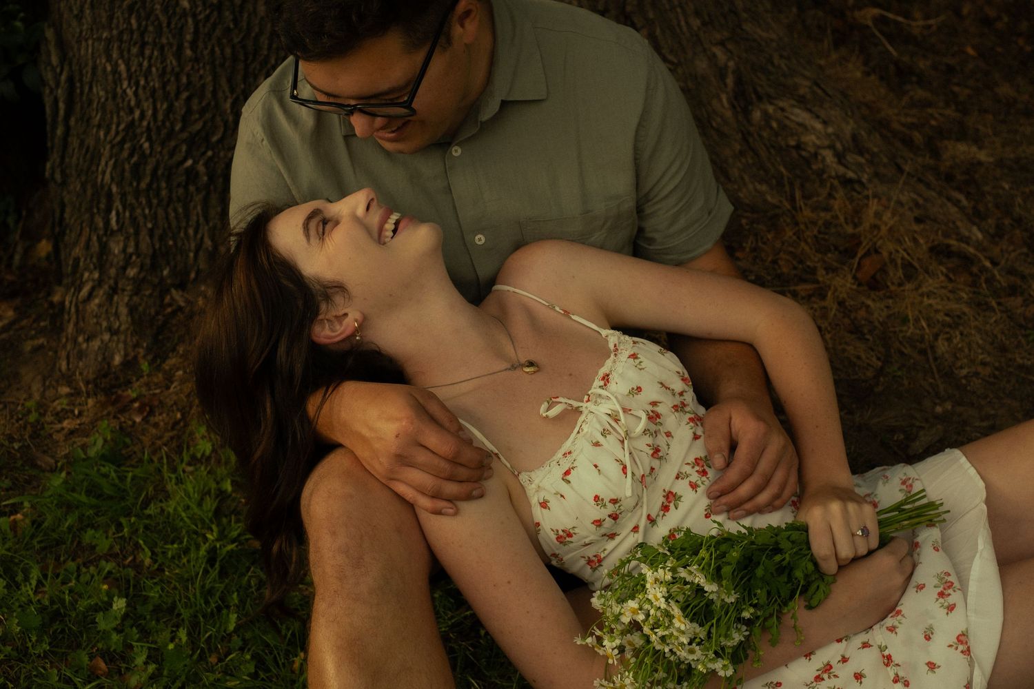 A romantic moment unfolds beneath a large tree in a scenic outdoor setting.