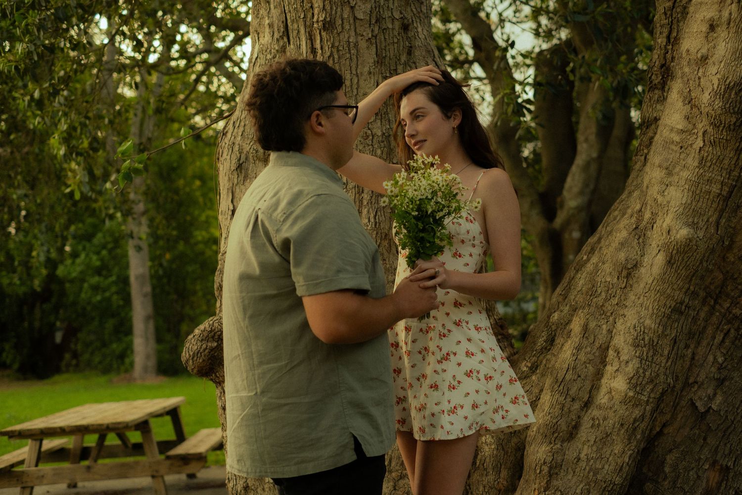 A tender embrace captured near a majestic old tree in a sunlit park.